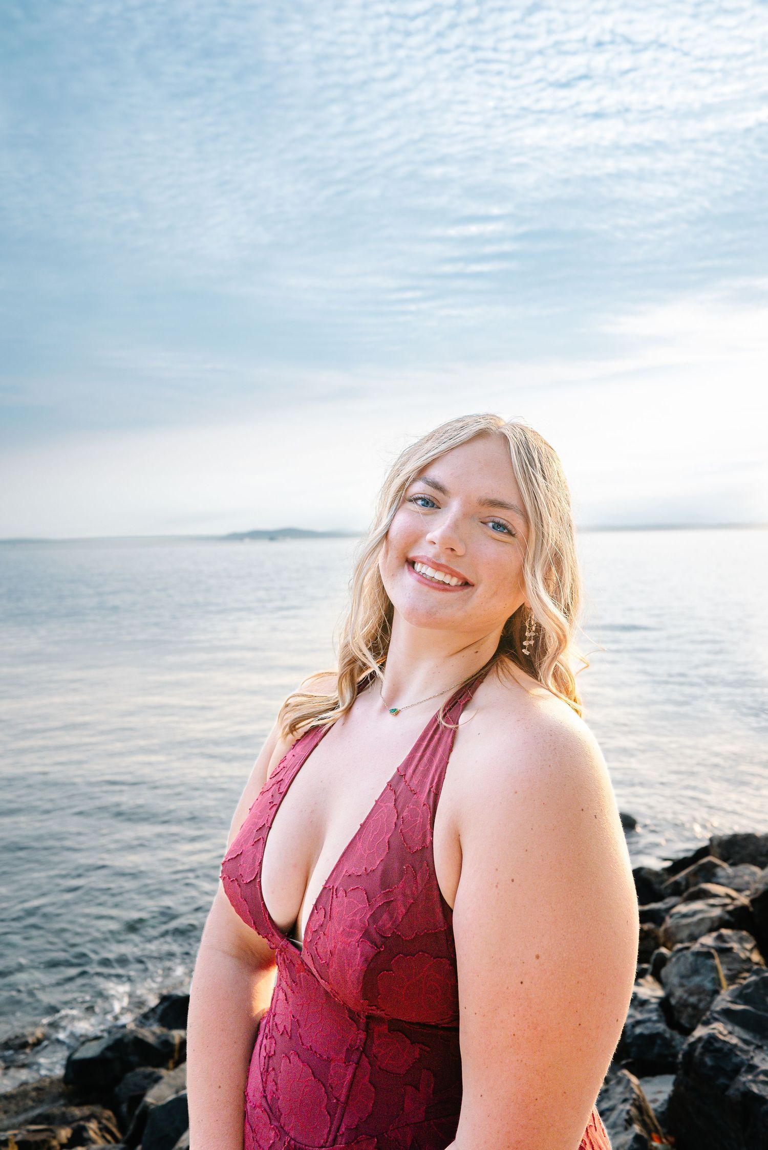 Smiling high school senior standing beside the rocky Elliott Bay shoreline in Seattle