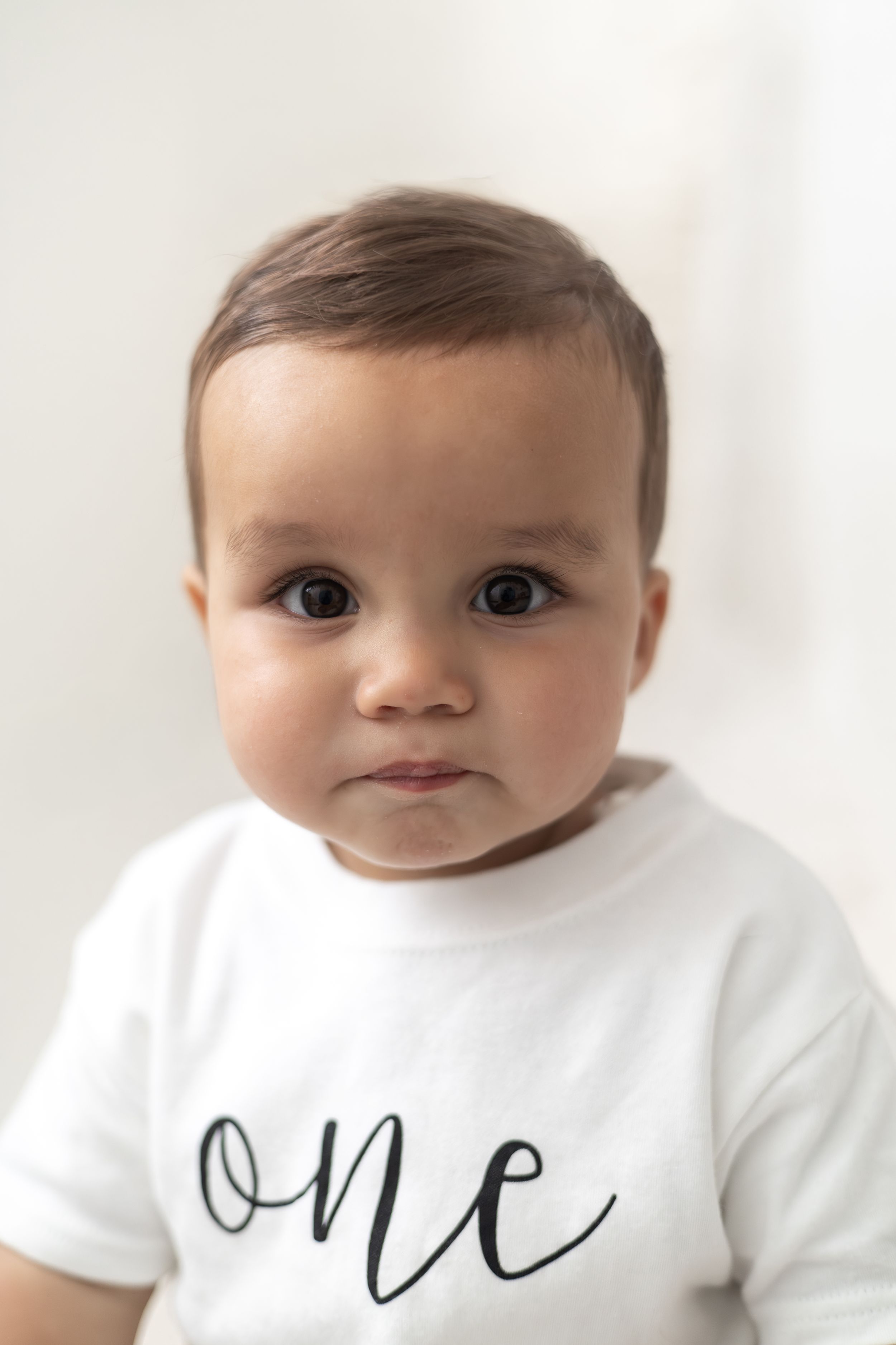 Cute baby wearing a white “one” shirt, celebrating their first birthday simple neutral first birthday shoot Nottingham