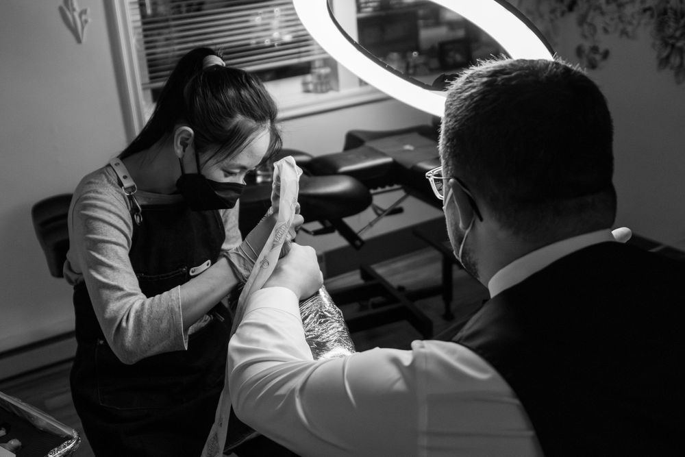 Tattooist works on a man's wedding ring tattoo while bathed in light from the light ring.