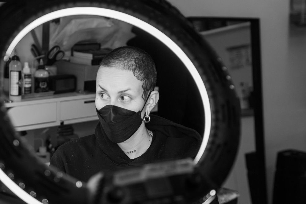 Black and white candid image of a tattoo artist as viewed through a light ring, as they work on a wedding ring tattoo.