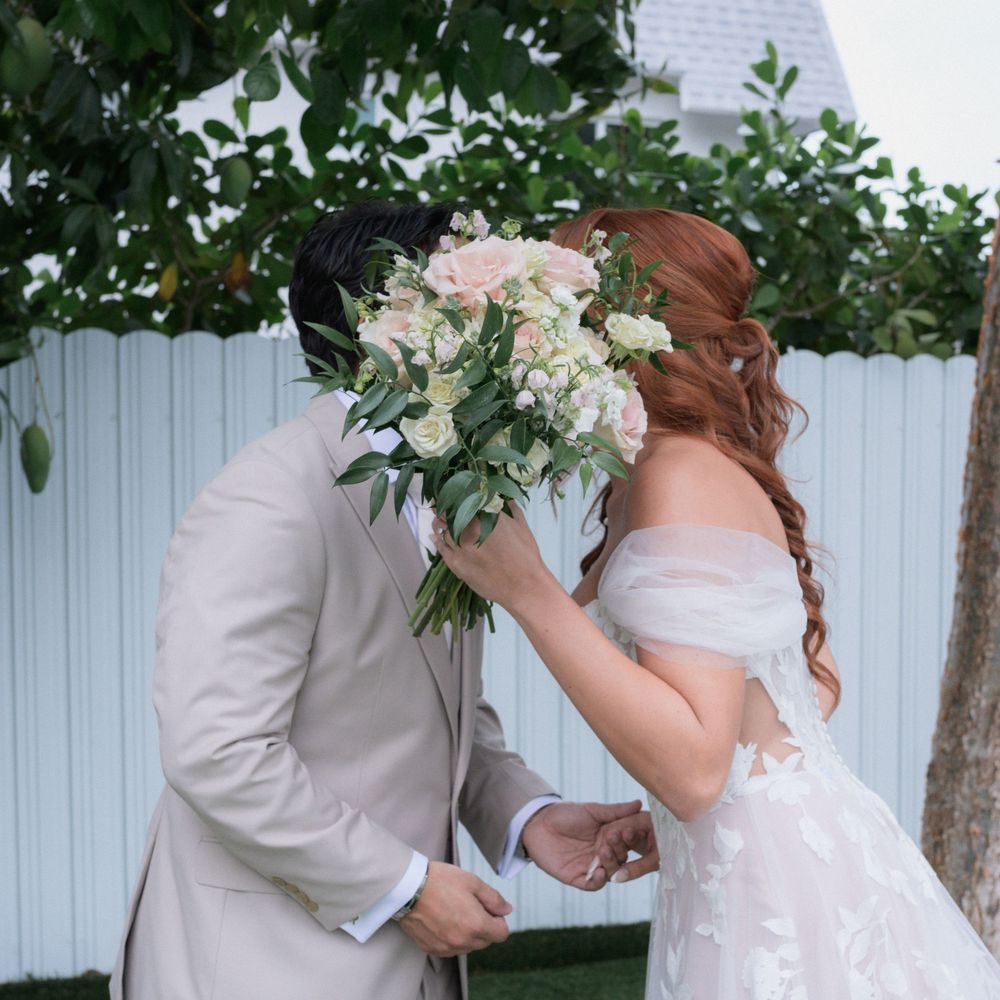 Bride and groom sharing a kiss hidden behind a beautiful blush and white rose wedding bouquet.