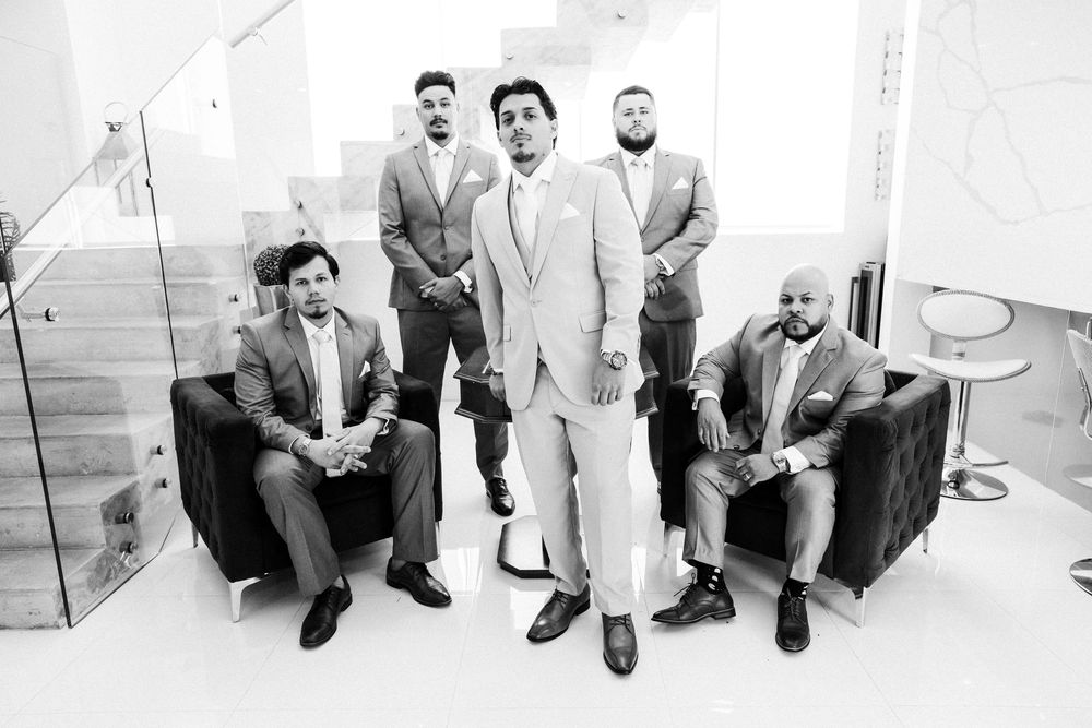Five men in suits pose elegantly in a modern white interior, with four seated and one standing in center.