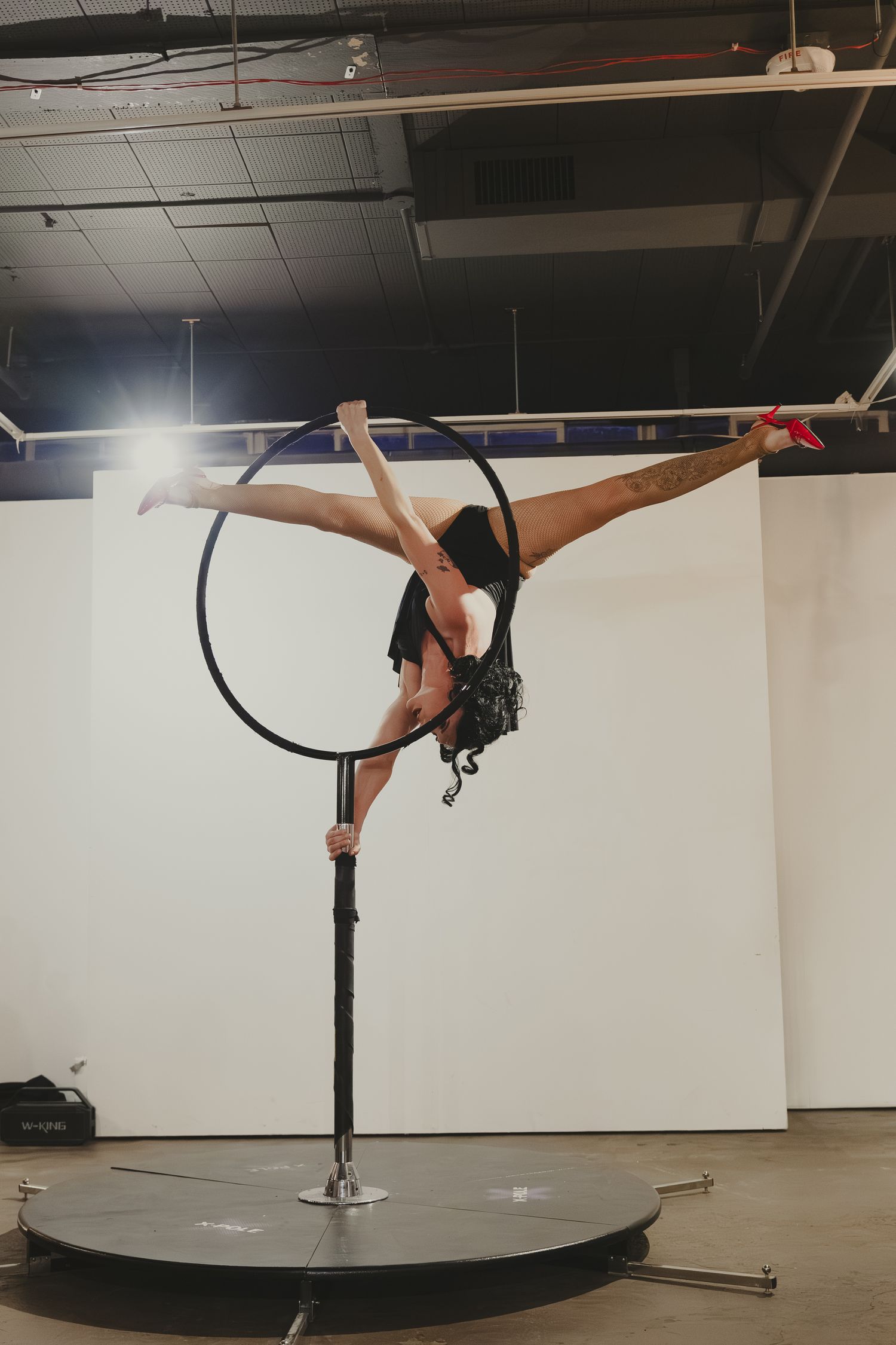 Aerial hoop performer executing a split on a lyra apparatus in a studio setting.