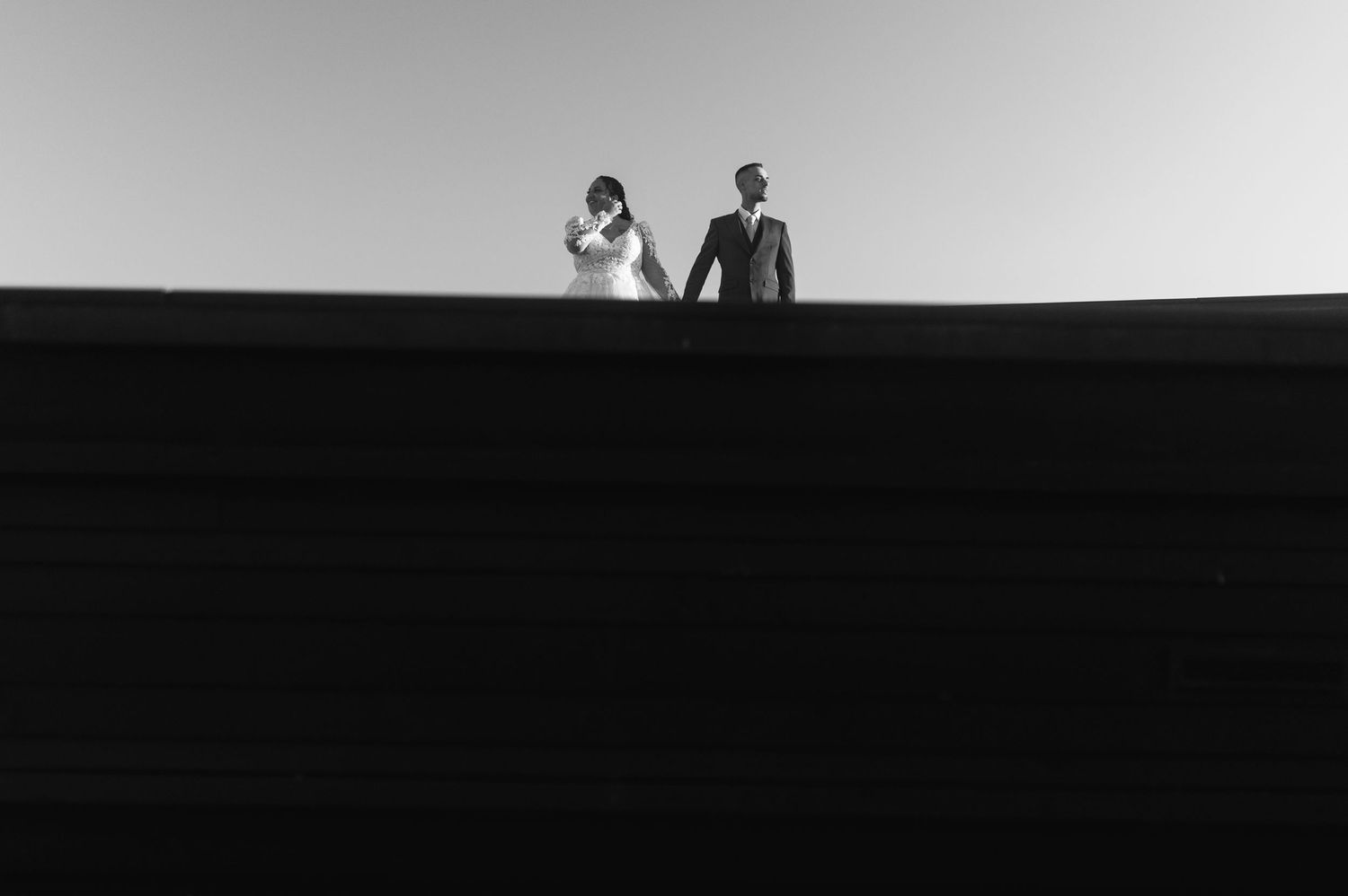 Black and white photo of a couple holding hands on a rooftop against a clear sky.