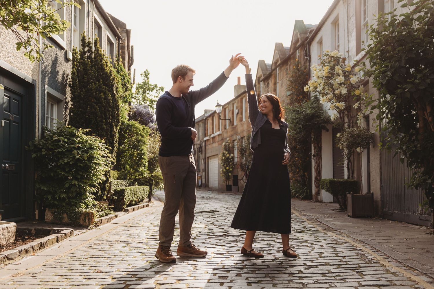 Couple dancing on a cobblestone street in London, surrounded by charming mews houses and lush greenery.