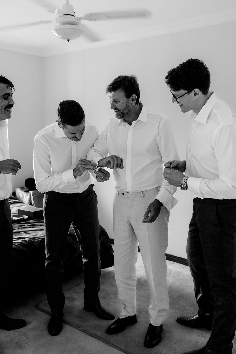 Black and white photo of groomsmen helping each other with cufflinks while getting ready for a wedding.
