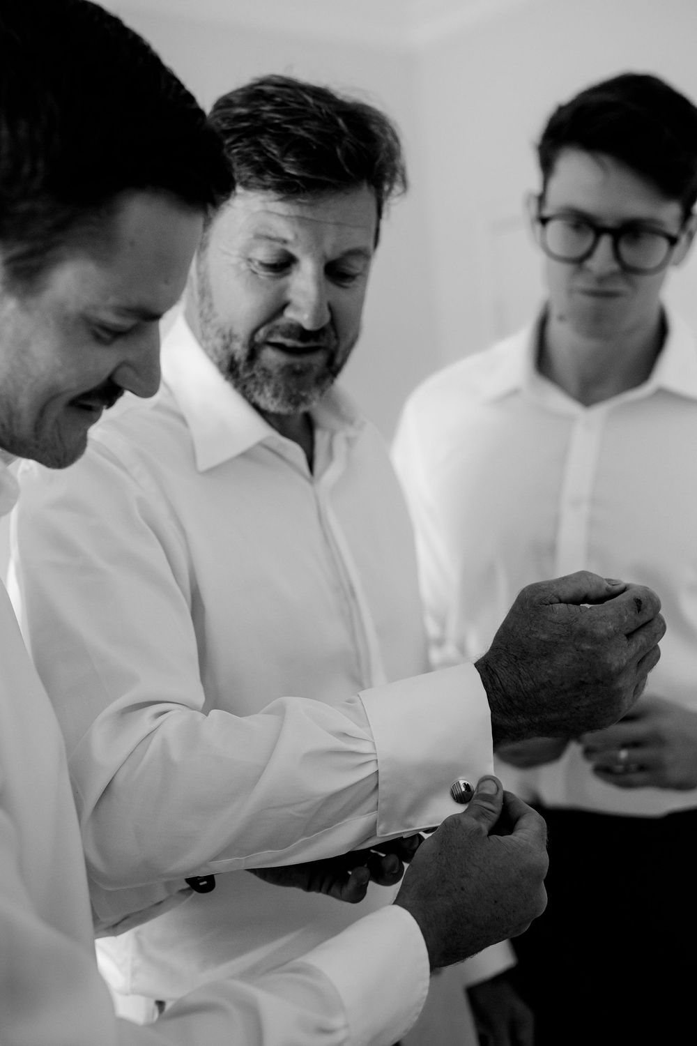 Black and white photo of three men in white shirts, one fastening cufflinks before a formal event.