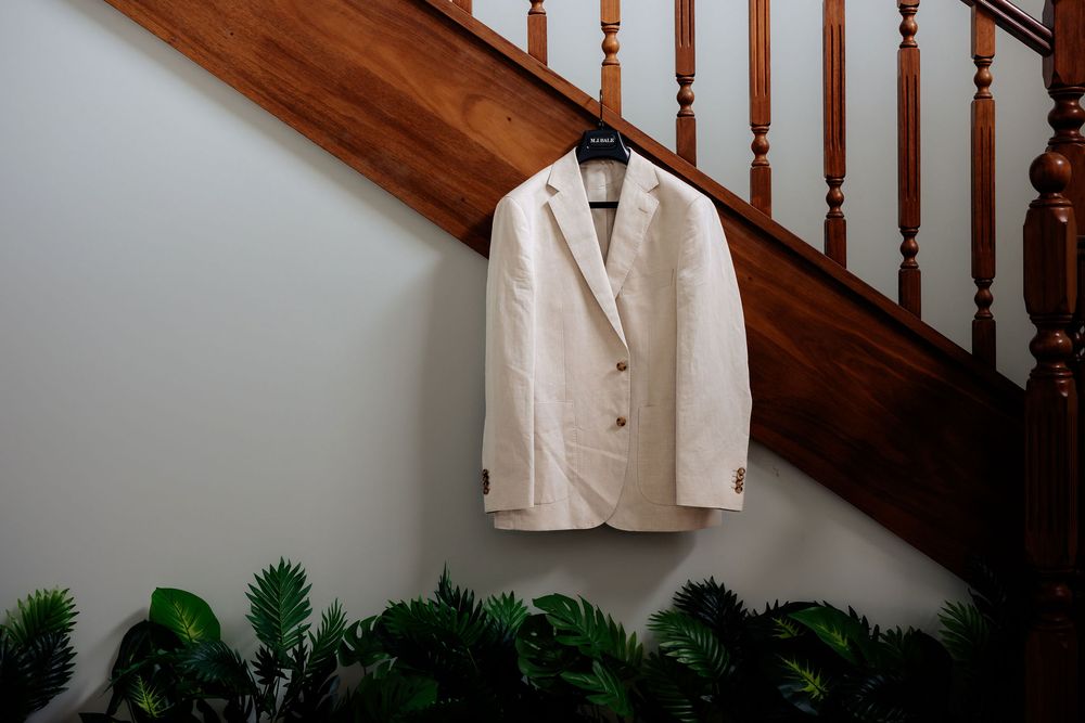 White blazer hanging on wooden staircase railing with green tropical plants below.