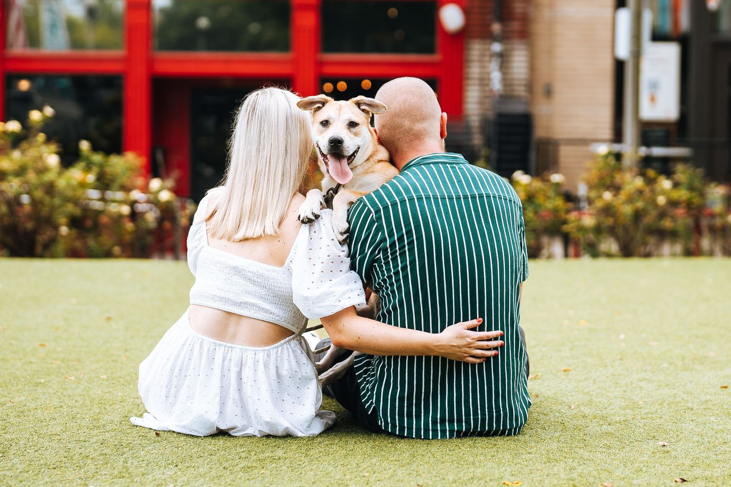 Couple in white and green outfits sitting together on grass in a garden setting.