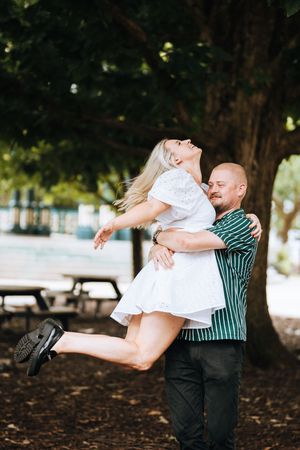 A romantic couple in a park share playful dance dips among trees and fallen leaves.