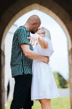 A couple in formal attire embraces under an arched walkway during a romantic photoshoot.