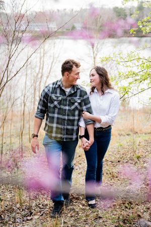 Couple holding hands and smiling at each other among spring blooms near a lake.