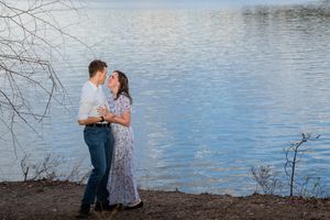 A couple shares a romantic moment by a serene lake, the woman in a floral dress gazing up at her partner.