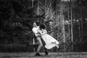 Black and white photo of a couple dancing outdoors near trees, the woman's dress flowing as they twirl together.