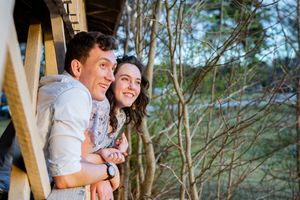 Happy couple embracing and smiling while standing on a wooden deck surrounded by trees outdoors.