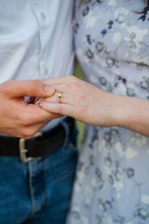 Close-up of a couple holding hands, woman wearing a gold engagement ring, man in jeans and white shirt.