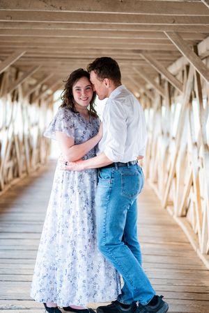 Couple dancing romantically in a wooden covered bridge, woman in floral dress, man in white shirt and jeans.