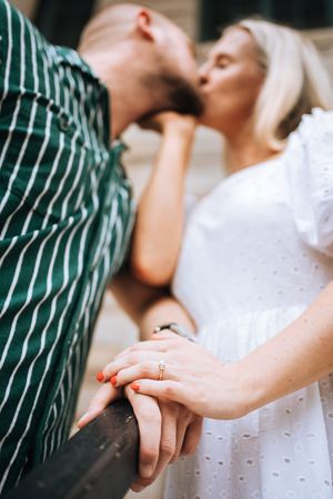 Close-up of hands with wedding rings touching as a couple shares an intimate moment in casual summer attire.