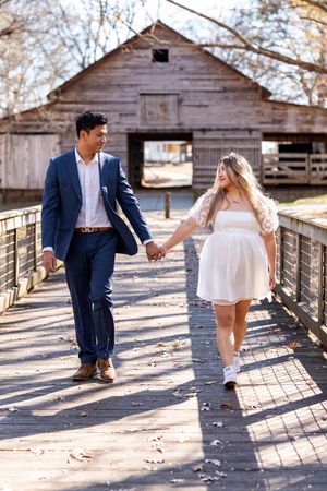 A couple shares a romantic moment on a wooden bridge walkway with rustic barns in the background on a sunny day.