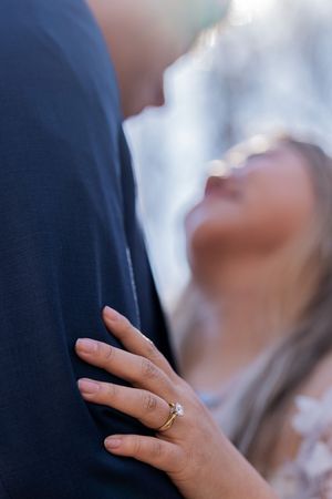 Close up shot of a hand wearing an engagement ring against a blurred blue background.