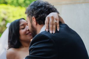 Bride smiling with groom showing off diamond engagement ring on wedding day.