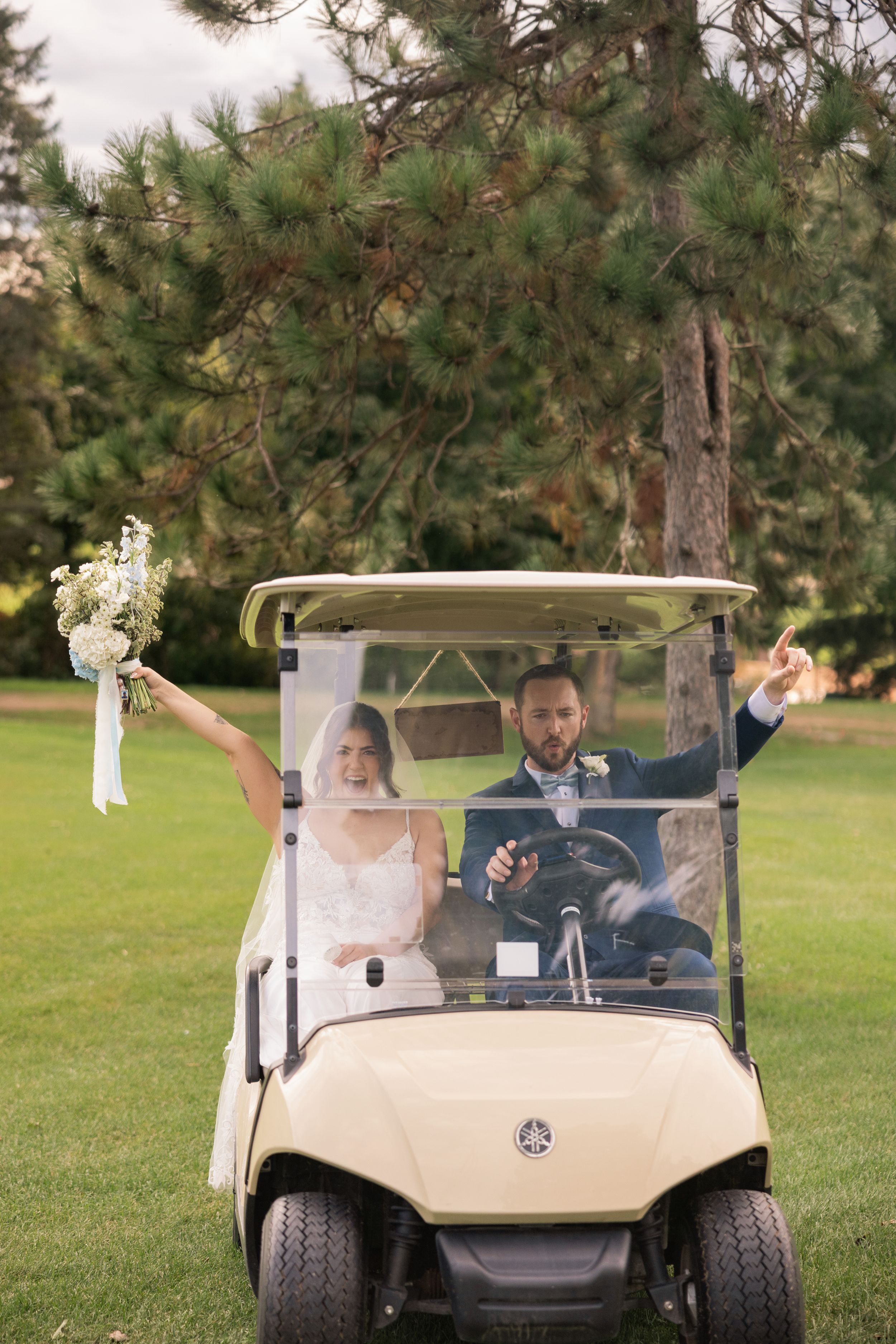 Bride and groom celebrating in a Yamaha golf cart on a green golf course, bride holding a white bouquet.