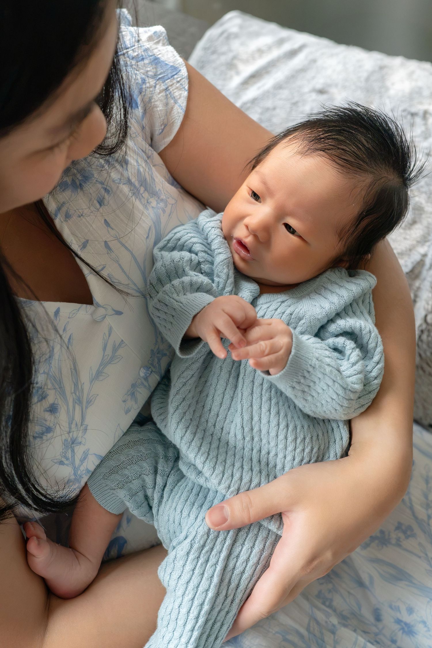 A mother tenderly holds her newborn baby dressed in a soft blue knit outfit while sitting on a bed.