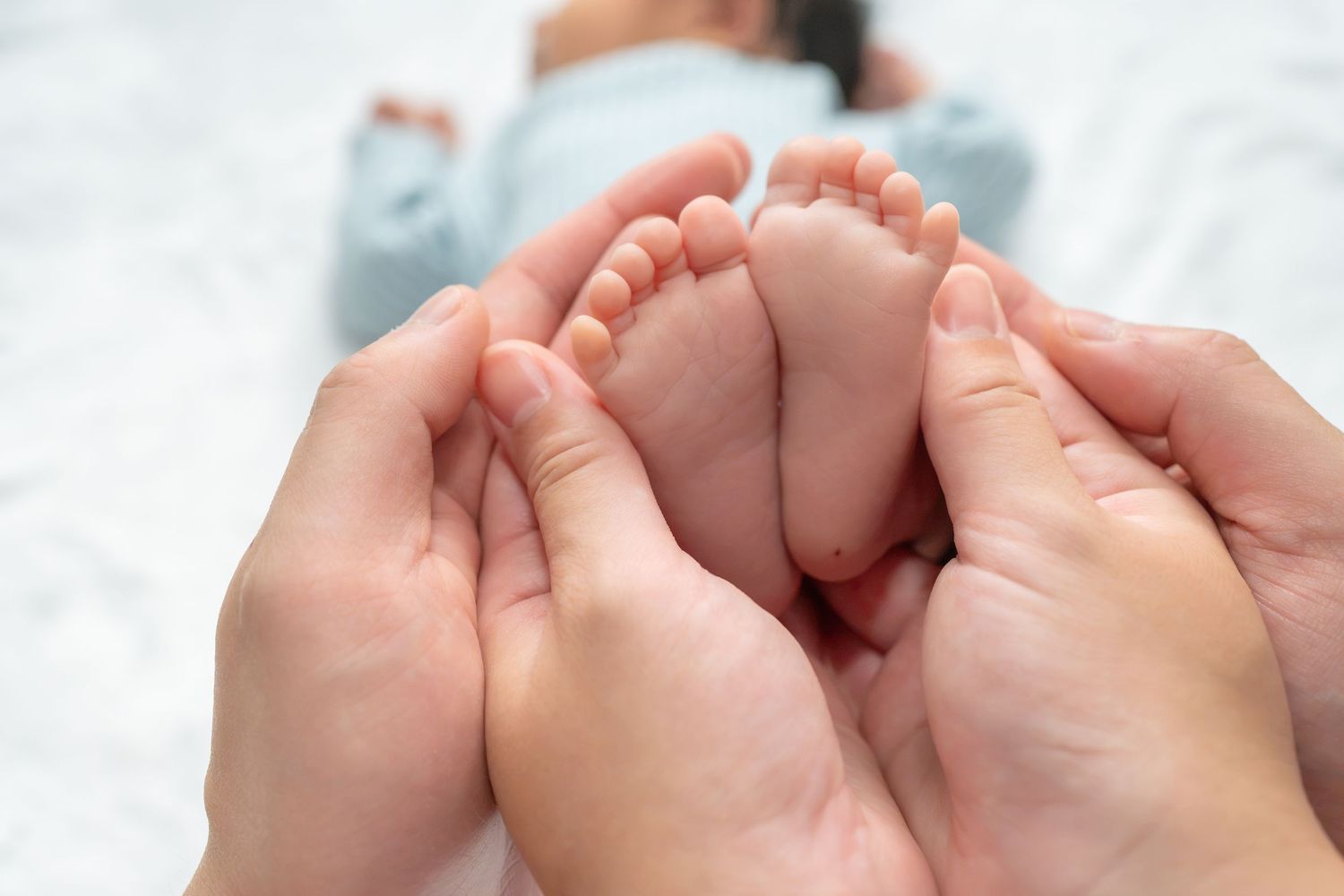 Adult hands gently cradling tiny newborn baby feet, showcasing the delicate bond between parent and child.