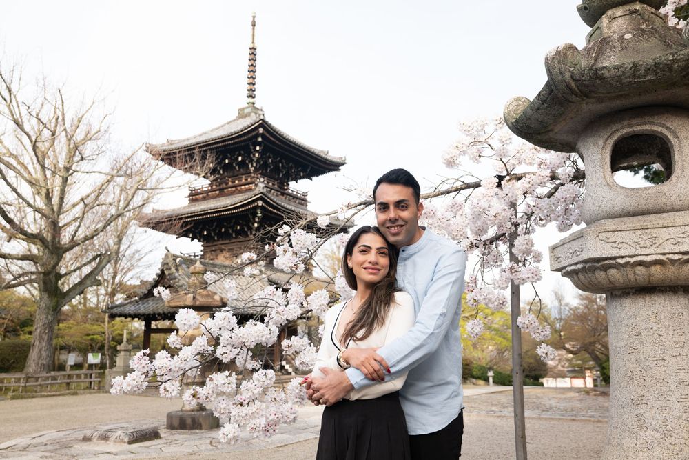 Couple embracing under blooming cherry blossoms in front of a traditional Japanese pagoda and stone lantern at a peaceful temple garden.