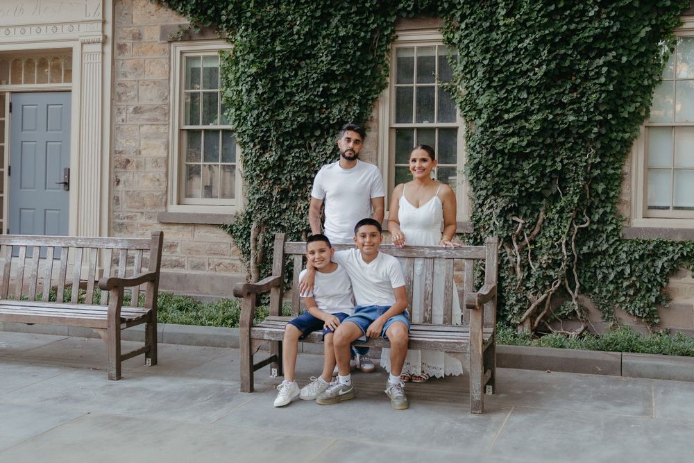 Family sitting together on a wooden bench outside an ivy-covered building in Princeton, NJ
