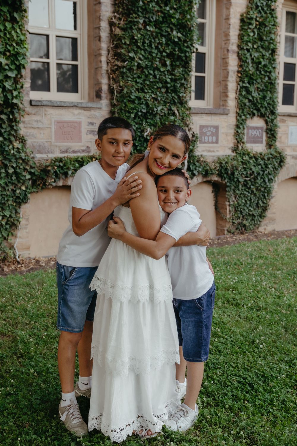 Mother hugging her two sons on the lawn beside ivy-covered walls, Princeton NJ family photos