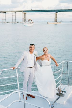Bride and groom posing on a yacht deck with ocean and bridge in the background.
