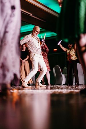 Bald man in white outfit dancing energetically at a wedding reception on the dance floor.