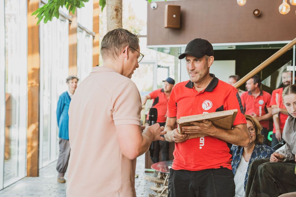 Two men in conversation outdoors, one in a red uniform holding a clipboard, the other in a pink shirt.