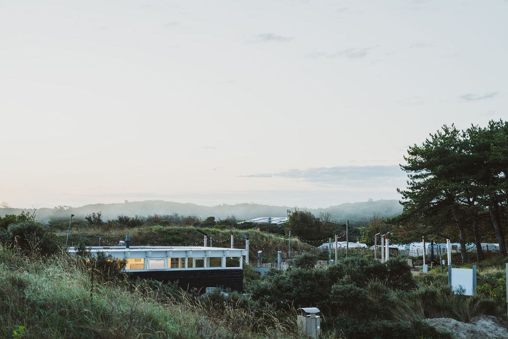 A modern white building nestled among lush green hills and trees at dusk with misty mountains in the background.