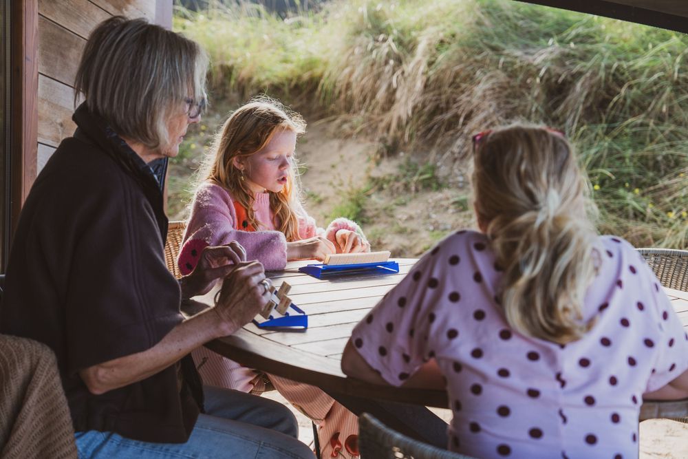 Two women and a young girl sit together at an outdoor wooden table, enjoying a warm sunny day at a rustic shelter.