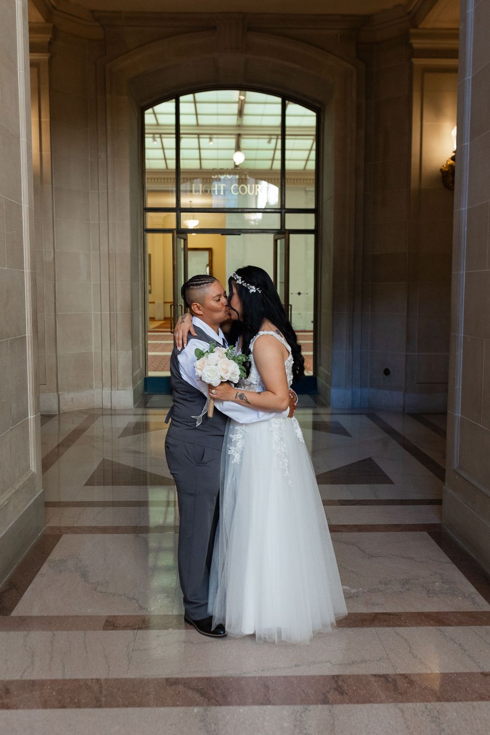 Newlyweds sharing a kiss in an elegant marble hallway, bride holding white bouquet.
