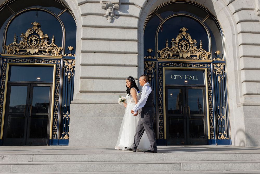 Couple in wedding attire posing on steps outside San Francisco City Hall with ornate gold doors.