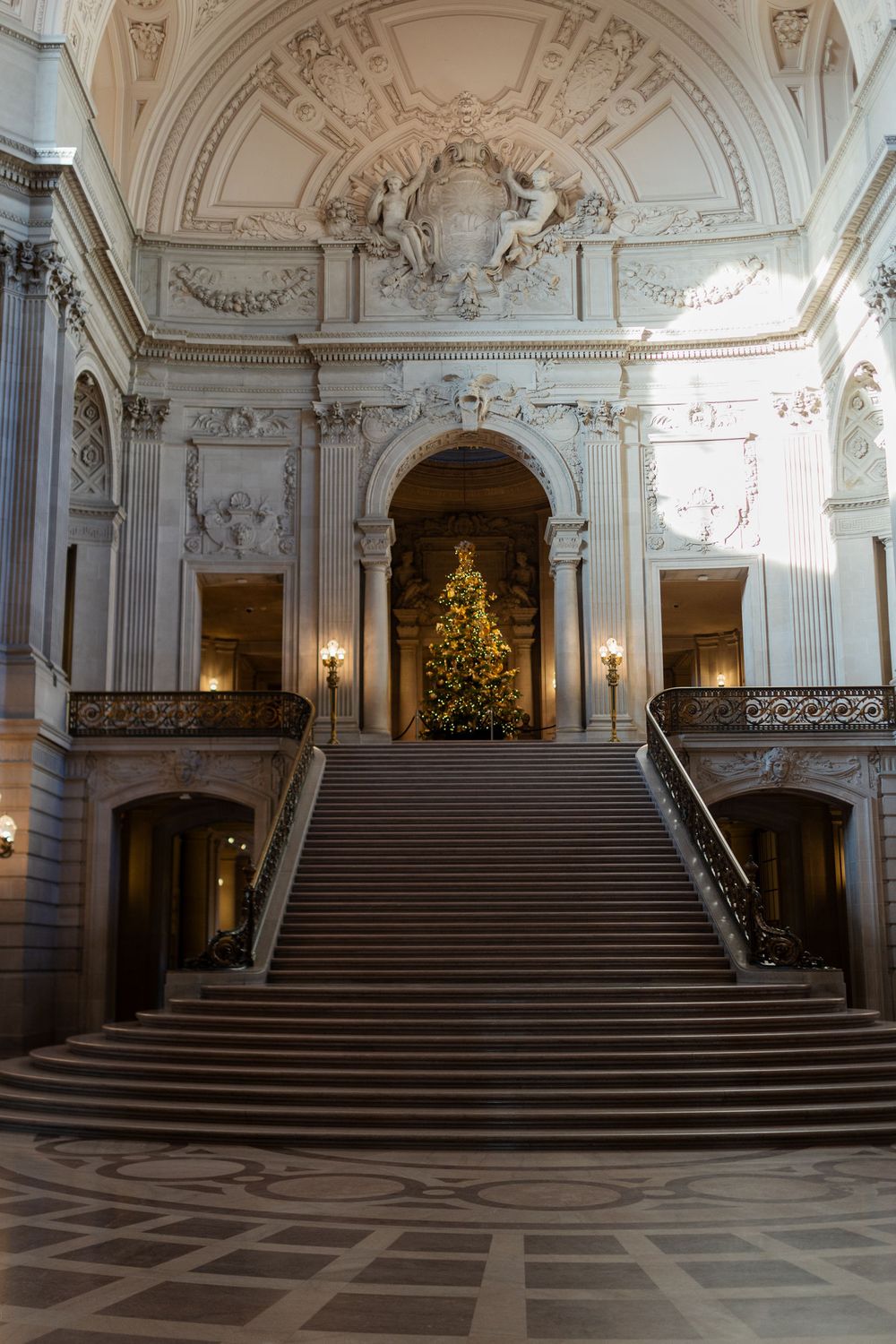 Grand staircase of San Francisco City Hall adorned with a lit Christmas tree, ornate Beaux-Arts architecture, and elegant marble floors.
