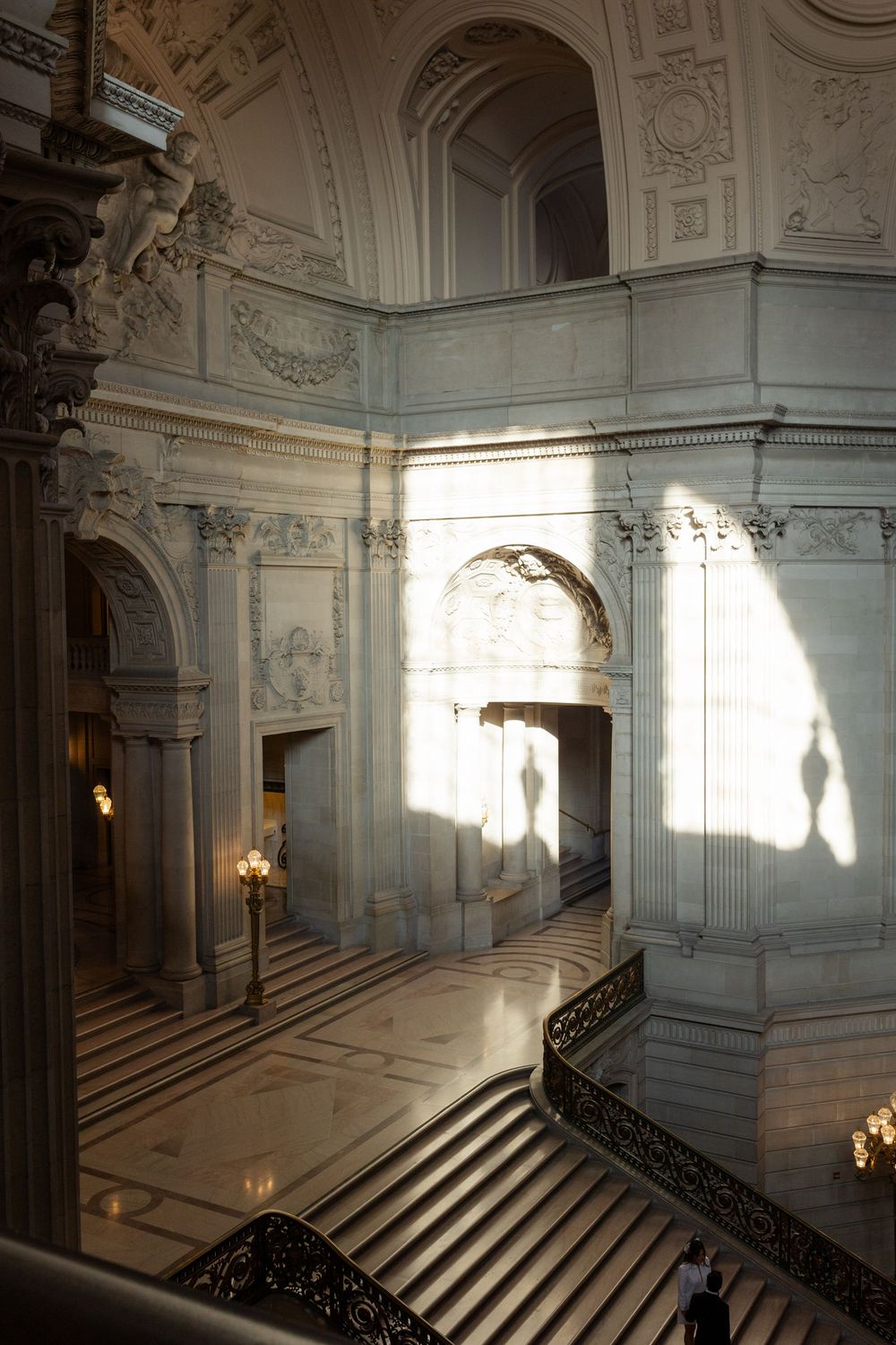 Sunlit grand marble staircase inside San Francisco City Hall with ornate railings and classical architectural details.