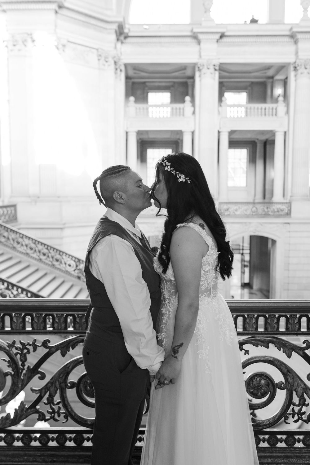 Newlywed couple sharing a kiss on the grand staircase of San Francisco City Hall in black and white.