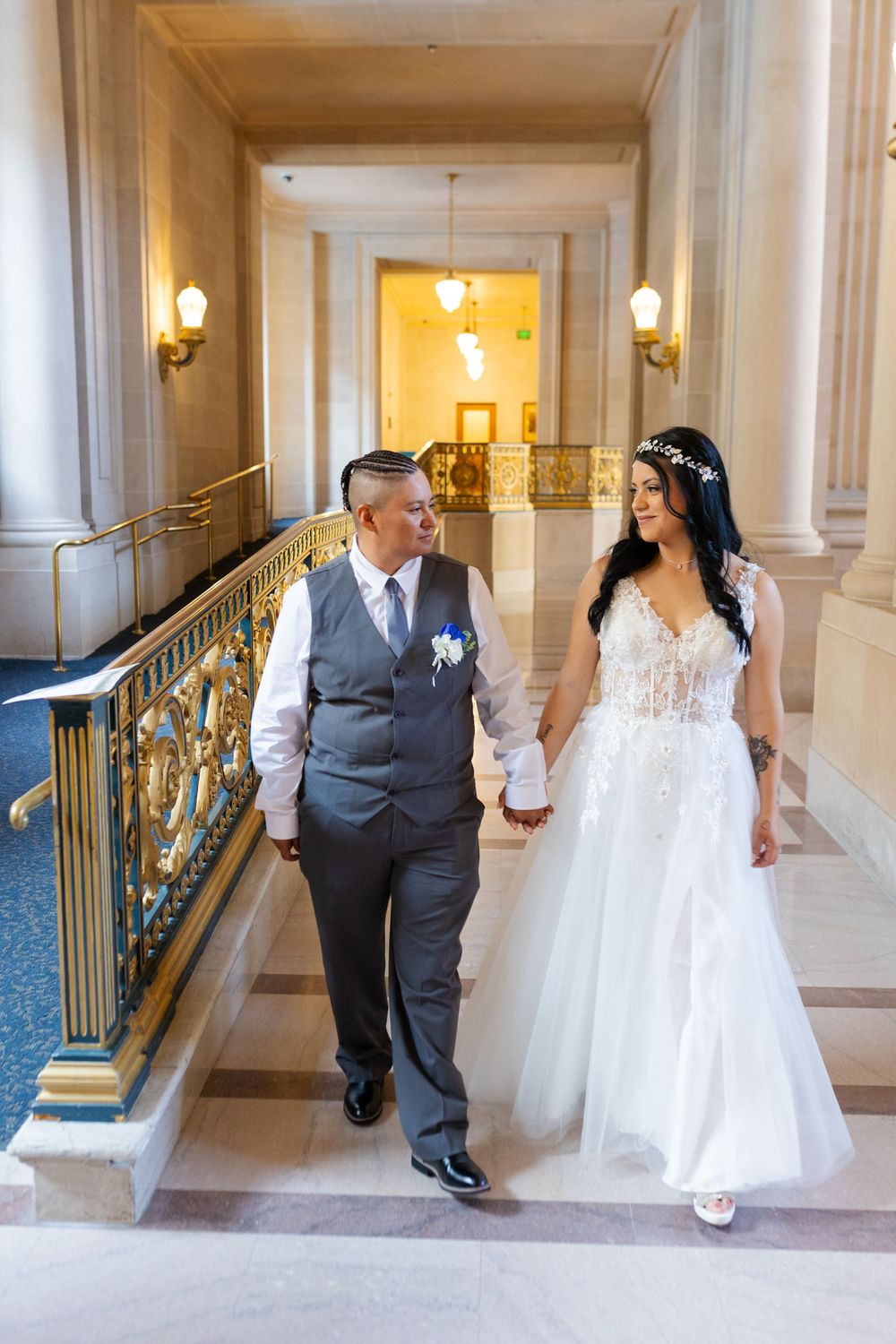 Bride and groom holding hands walking up marble stairs at San Francisco City Hall on their wedding day.