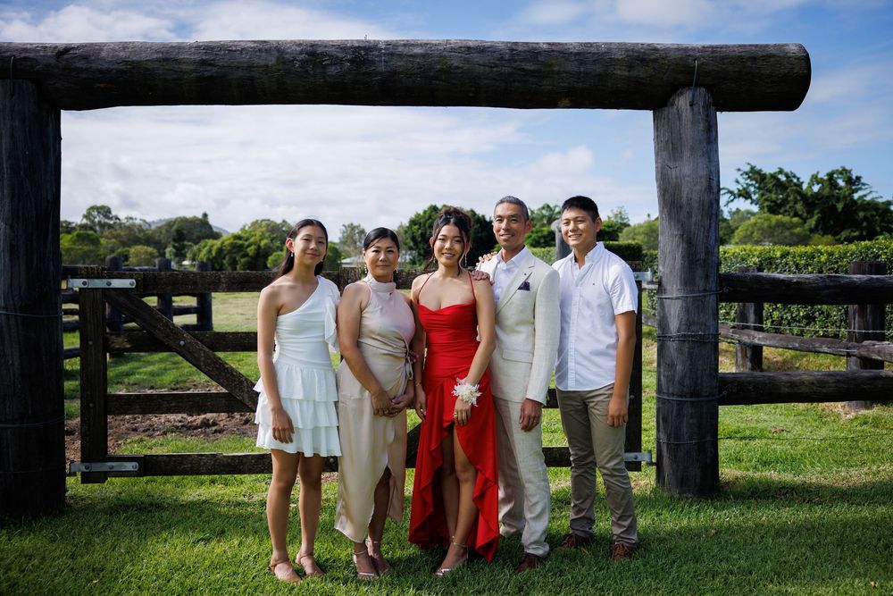 Family of five dressed in formal wear, including a woman in a red gown, stand under a rustic wooden gateway.