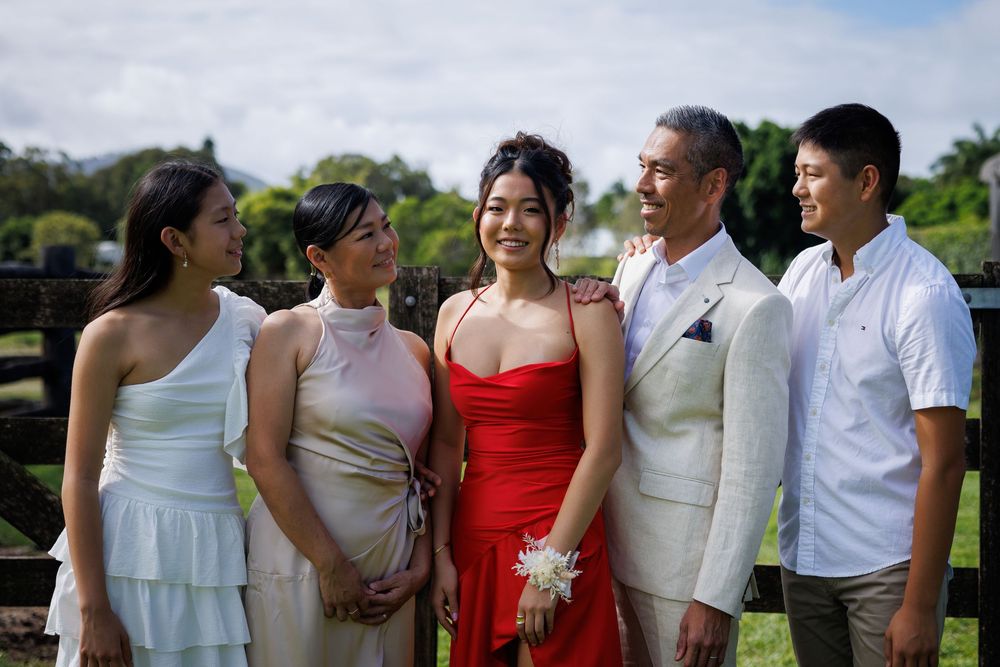 Smiling family of five in formal outfits, with a young woman in a red dress and corsage, pose outdoors on green grass.