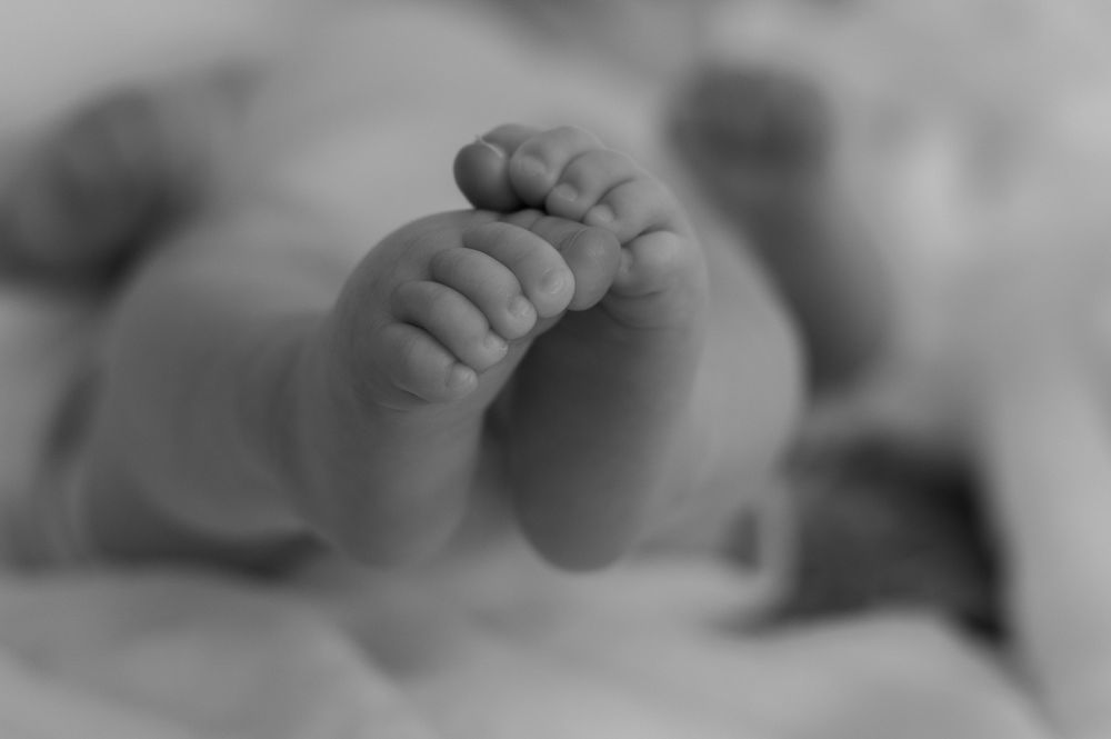 Black and white close-up of a newborn baby's tiny feet and toes with a soft, blurred background.