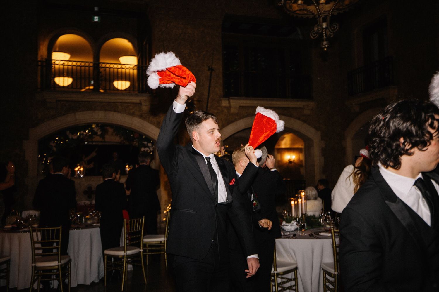 Groomsmen wave Santa hats overhead in a candlelit hall at a Fairmont Banff Springs wedding reception