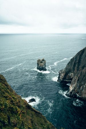 Lone sea stack rock formation surrounded by rough ocean waves viewed from coastal cliffs.