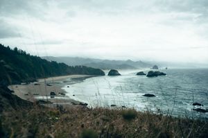 Panoramic view of Oregon coast with sea stacks, sandy beach, and misty mountains.