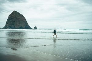 Person walking along a misty beach with iconic Haystack Rock at Cannon Beach, Oregon.