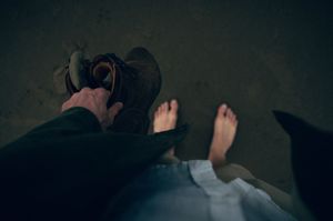 Overhead view of two people standing barefoot and in boots on dark sand beach.